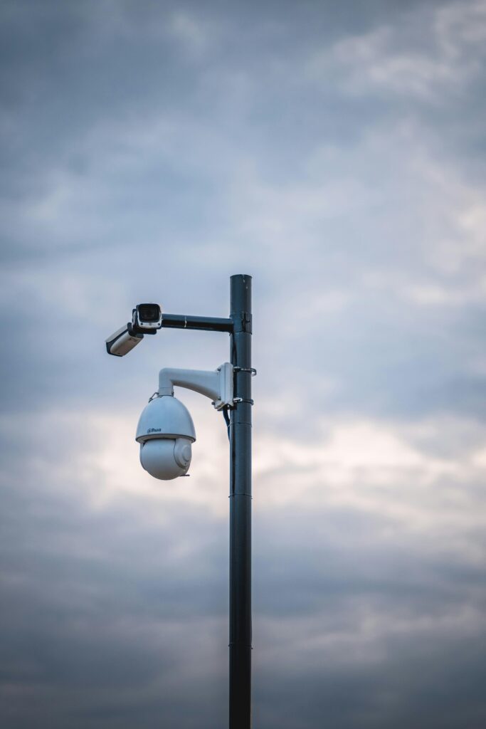 Security cameras mounted on a pole under a cloudy sky emphasize surveillance and protection.